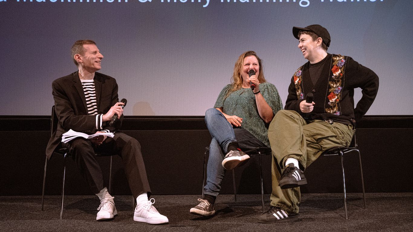 Molly Manning-Walker, Ivana MacKinnon and Danny Leigh sit on stage during a panel discussion. Molly speaks into a microphone while Ivana listens with a smile.